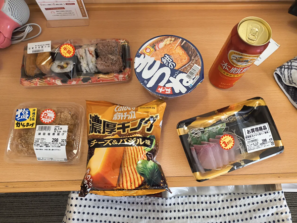 生成AIに送った夕食の写真。スーパーで買った助六寿司、からあげ、ぶりの刺身、カップそばなどが並んでいる